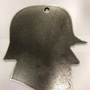 Peut inclure: Une silhouette métallique d'une personne portant un casque. La silhouette est de couleur gris foncé et a un trou en haut pour accrocher.