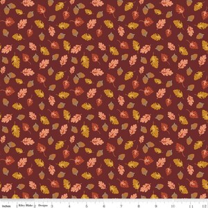 May include: A fabric print featuring a repeating pattern of autumn leaves and acorns in shades of orange, yellow, and brown against a dark maroon background, with a white ruler at the bottom measuring 12 inches by Riley Blake Designs.