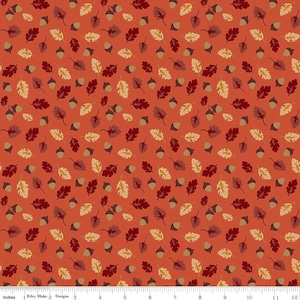 May include: A fabric print featuring a repeating pattern of acorns and oak leaves in shades of cream, dark red, and brown against a solid burnt orange background, with a visible 12-inch ruler along the bottom edge for scale reference.