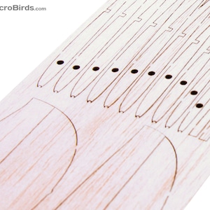 Puede incluir: Primer plano de una pieza artesanal de madera clara con l&iacute;neas grabadas y peque&ntilde;os agujeros. El dise&ntilde;o incluye formas curvas y l&iacute;neas paralelas, posiblemente para un proyecto de bricolaje o modelado. El texto "MicroBirds.com" est&aacute; en la esquina superior izquierda.