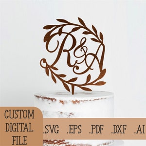 Può includere: Un topper per torta in legno marrone con un design a corona di foglie e le lettere "R & A" in un font corsivo.