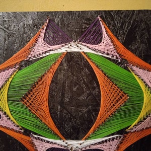May include: Abstract art created with colorful string wrapped around nails on a black canvas. The string is arranged in a geometric pattern with a central oval shape.