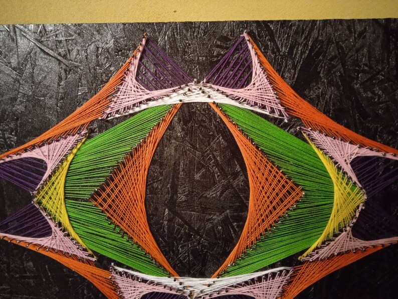 May include: Abstract art created with colorful string wrapped around nails on a black canvas. The string is arranged in a geometric pattern with a central oval shape.