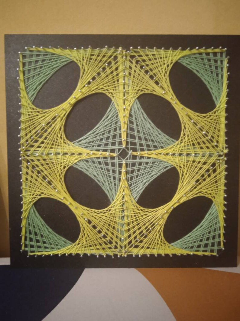 May include: A geometric string art piece with a black background. The design features four overlapping circles created with yellow and green string.
