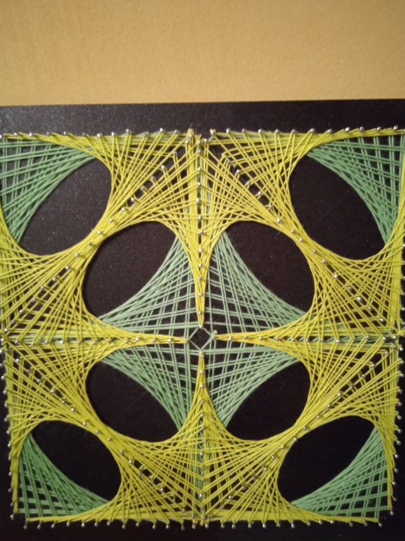 May include: A geometric string art piece with a black background and a design of four overlapping circles. The circles are outlined in yellow string and filled in with green string.