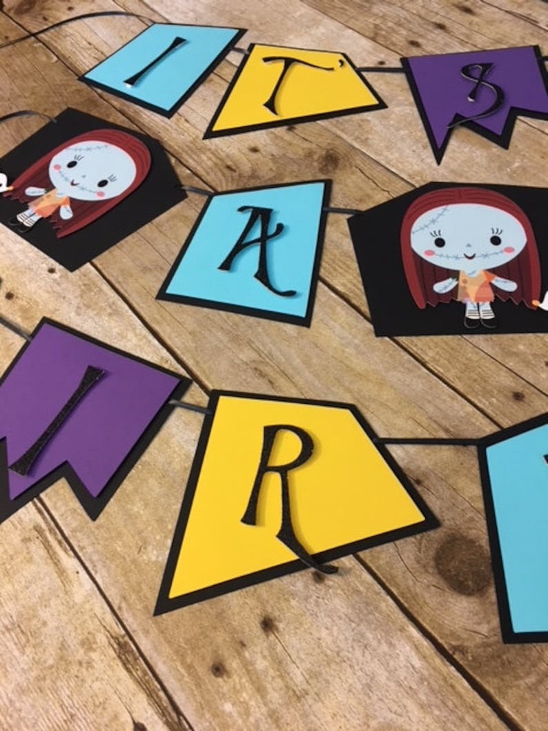 Op de afbeelding: Een kleurrijk spandoek met de woorden "It's a Party" in zwarte letters op verschillende gekleurde achtergronden. Het spandoek toont twee personages uit de film "Nightmare Before Christmas" met gestikte gezichten en rood haar.