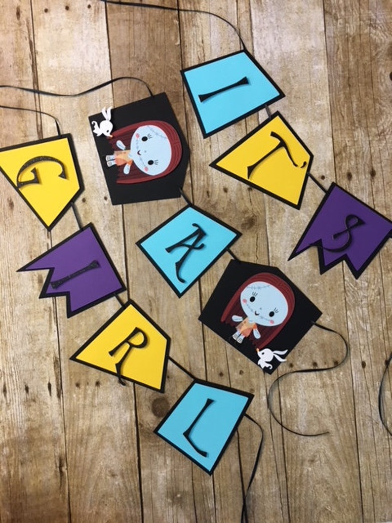 Op de afbeelding: Een kleurrijk spandoek met het woord "GIRL" gespeld in zwarte letters op gele, paarse en blauwe ruitvormige papieren uitsnijdingen. De banner bevat ook twee afbeeldingen van Sally uit The Nightmare Before Christmas.
