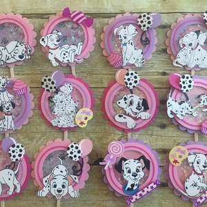 May include: Twelve pink and purple cupcake toppers featuring Dalmatian puppies with confetti and balloons. The toppers are perfect for a Dalmatian-themed party.