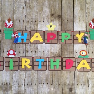 May include: A colourful banner with the words "Happy Birthday" in a brick pattern. The banner features characters from the video game Super Mario Bros., including Mario, Luigi, and a Goomba.