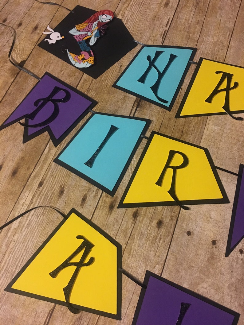 Op de afbeelding: Een kleurrijk papieren banner met de woorden "Happy Birthday" in zwarte letters. De banner is versierd met een zwart silhouet van Sally uit The Nightmare Before Christmas.