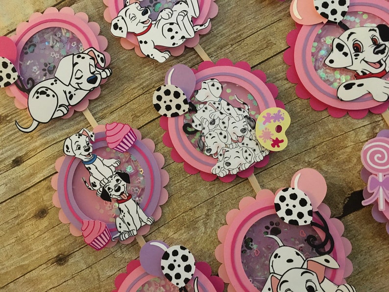 May include: Set of 6 Dalmatian themed cupcake toppers. Each topper features a different Dalmatian design with pink, purple, and white accents. The toppers are perfect for a Dalmatian themed party.
