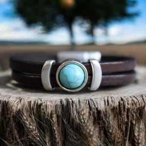 May include: A brown leather bracelet with a silver buckle and a turquoise stone in the center.
