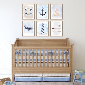May include: A wooden crib with a blue and white striped mattress and a blue and white striped skirt. The crib is decorated with six framed prints featuring nautical themes, including an anchor, a sailboat, a whale, a lighthouse, oars, and a life preserver with the text "Welcome Aboard".