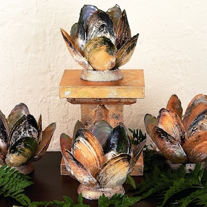 May include: Four decorative lotus flower candle holders made from iridescent seashells. The candle holders are arranged on a wooden stand and a dark surface.