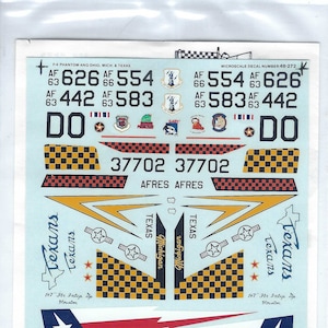 Puede incluir: Una hoja de calcomanías para un modelo de avión con un patrón a cuadros, las palabras "Texans" y "U.S. Air Force", y los números "37702", "626", "554", "442", y "583".