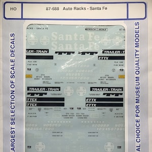 Puede incluir: Una hoja de calcomanías para trenes modelo que presenta el logotipo de Santa Fe Railway y varias marcas. Las calcomanías están impresas en un fondo blanco con letras azules y negras. La hoja incluye el texto "Trailer Train", "TTGX", "ETTX", "ATSF" y "Santa Fe".
