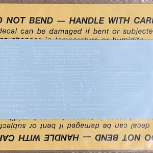 May include: A yellow and blue decal with the text "DO NOT BEND - HANDLE WITH CARE" printed on it. The decal is for a boxcar and includes information about the boxcar's capacity, weight, and other features. The text "PRODUCE VENTILATED" is repeated multiple times on the decal.