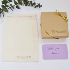 Peut inclure: Un petit sac en mousseline blanche avec un cordon rouge et le texte "Little Happies Co." imprim&eacute; au bas. Une bo&icirc;te brune avec un ruban dor&eacute; et le texte "Little Happies Co." imprim&eacute; sur le dessus. Une carte violette avec le texte manuscrit "Avec amour, Anna".