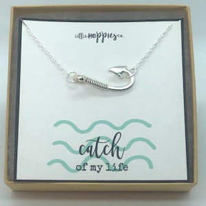 May include: A silver necklace with a fishing hook charm and a card that says "catch of my life" in a light blue and white design.