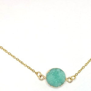 May include: A delicate gold chain necklace with a round, light green gemstone pendant.