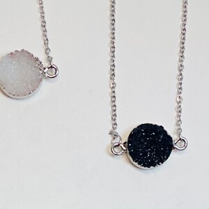 May include: Two silver necklaces with round, textured pendants. One pendant is white and the other is black.