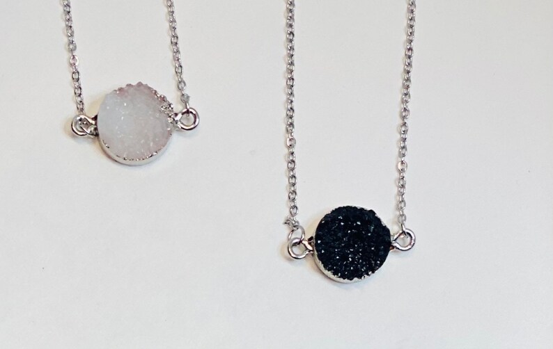May include: Two silver necklaces with round, textured pendants. One pendant is white and the other is black.