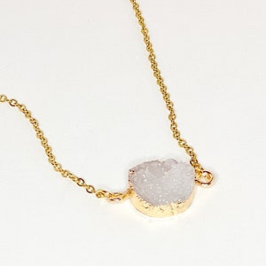 May include: A delicate gold chain necklace with a white crystal pendant. The crystal is a natural, raw, and irregular shape.