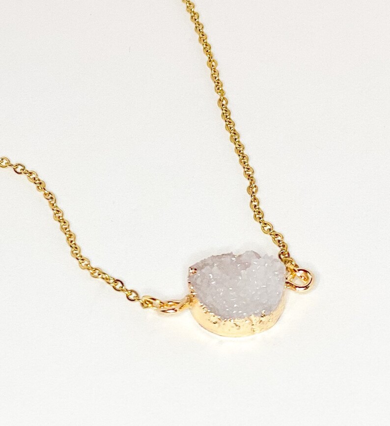 May include: A delicate gold chain necklace with a white crystal pendant. The crystal is a natural, raw, and irregular shape.