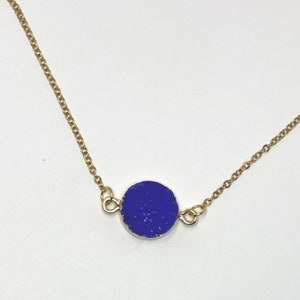 May include: A gold chain necklace with a round, dark blue pendant.