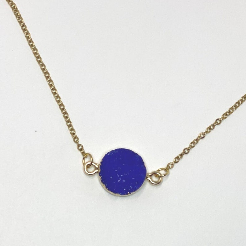 May include: A gold chain necklace with a round, dark blue pendant.