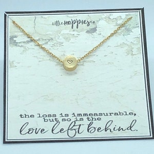 May include: A gold necklace with a small round pendant featuring a heart design. The necklace is displayed on a card with the text "the loss is immeasurable, but so is the love left behind."