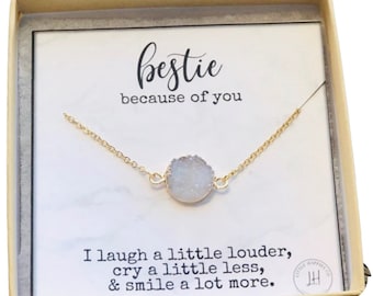 Peut inclure: Un collier avec un petit pendentif en pierre blanche et une chaîne dorée dans une boîte cadeau. La boîte contient une carte qui dit "bestie because of you" et "I laugh a little louder, cry a little less, & smile a lot more."