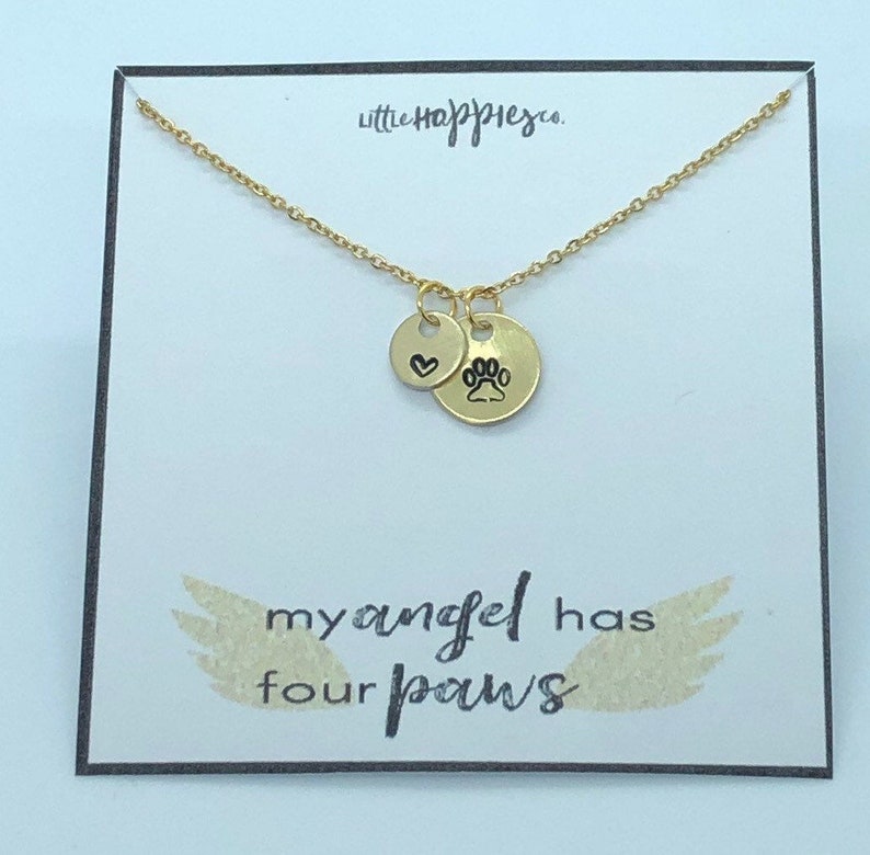 Puede incluir: Collar de oro con dos dijes, un coraz&oacute;n y una huella de pata. El collar est&aacute; sobre una tarjeta blanca con el texto "my angel has four paws".