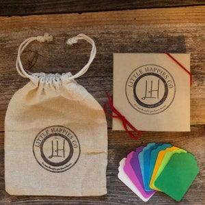 Puede incluir: Un conjunto de etiquetas de regalo coloridas con una bolsa de papel marr&oacute;n y una caja con el texto "Little Happies Co." impreso en ella. Las etiquetas de regalo son de varios colores, incluyendo morado, azul, verde, amarillo y naranja.