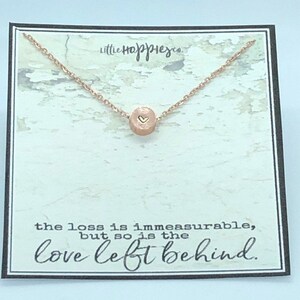 May include: A rose gold necklace with a small round pendant featuring a heart design. The necklace comes on a card with the text "the loss is immeasurable, but so is the love left behind."