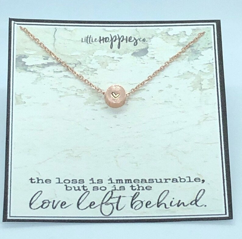 May include: A rose gold necklace with a small round pendant featuring a heart design. The necklace comes on a card with the text "the loss is immeasurable, but so is the love left behind."