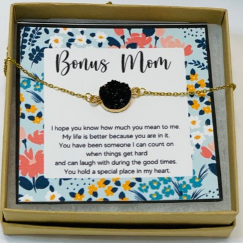 May include: A gold chain necklace with a black stone pendant in a gift box. The box has a card inside that reads "Bonus Mom" and a message about how much the recipient means to the giver.