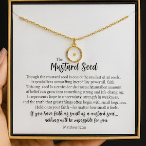 May include: Gold-colored necklace with a mustard seed pendant, presented in a gift box. The pendant features a small, round, clear casing with a tiny yellow seed inside. The box has text about faith.