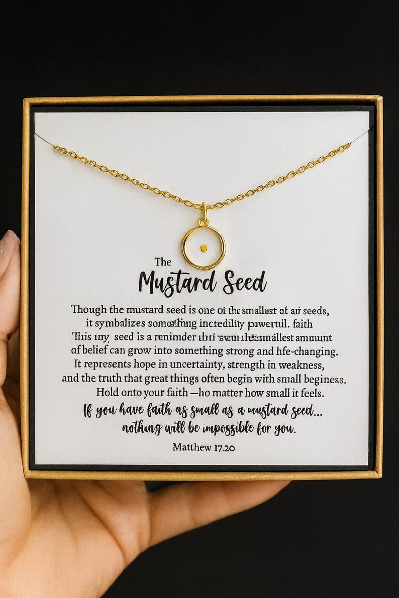 May include: Gold-colored necklace with a mustard seed pendant, presented in a gift box. The pendant features a small, round, clear casing with a tiny yellow seed inside. The box has text about faith.