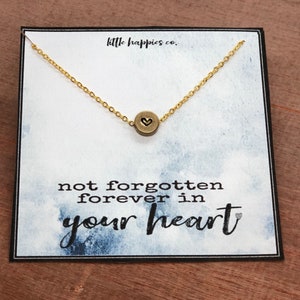 May include: A gold necklace with a small heart charm on a white card with the text "not forgotten forever in your heart".