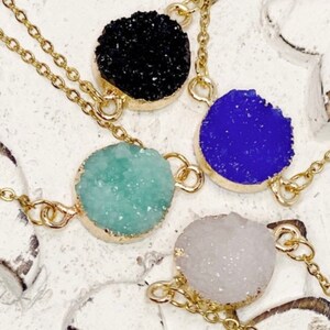 May include: Four gold chain necklaces with different colored crystal pendants. The pendants are round and have a rough, textured surface. The colors are black, blue, green, and white.