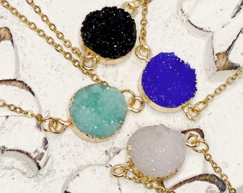 May include: Four gold chain necklaces with different colored crystal pendants. The pendants are round and have a rough, textured surface. The colors are black, blue, green, and white.