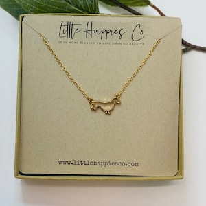 Peut inclure: Collier en or en forme de dachshund dans une petite bo&icirc;te en carton avec le texte "Little Happies Co. Il est plus b&eacute;ni de donner que de recevoir" et le site web "www.littlehappiesco.com".