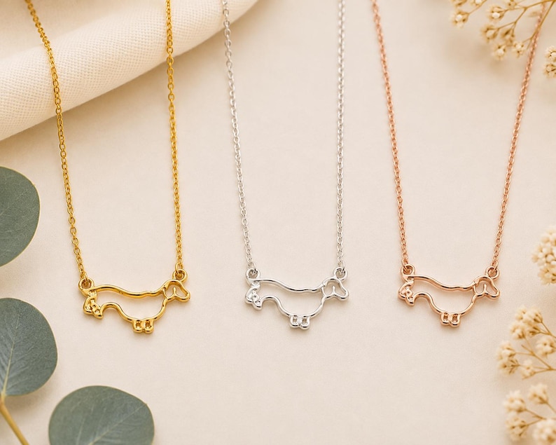 May include: Three necklaces featuring a minimalist outline pendant of a dachshund dog. The set includes one gold-toned necklace, one silver-toned necklace, and one rose gold-toned necklace, each with a delicate chain and a dog-shaped charm.