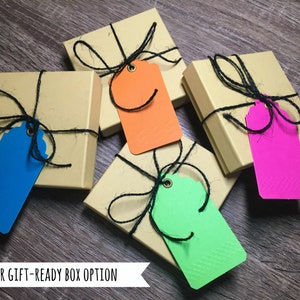 May include: Four small, square, brown gift boxes with black string and bows. Each box has a colorful tag attached: blue, orange, green, and pink.