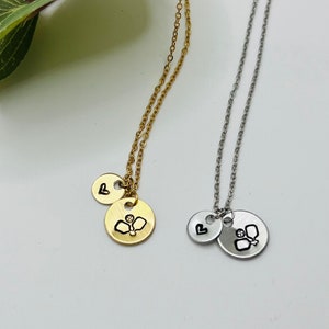 May include: Two necklaces with a heart charm and a charm with a paddle and ball design. One necklace is gold and the other is silver.