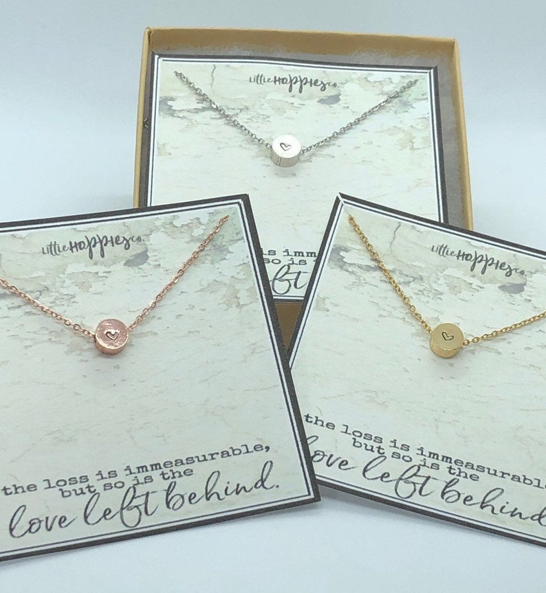 May include: Three necklaces with small heart charms on a white background. The necklaces are silver, gold, and rose gold. The necklaces are in boxes with the text "Little Happier" and the quote "The loss is immeasurable, but so is the love left behind."