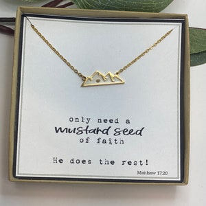 May include: A gold necklace with a small mountain charm and a white card with the text "only need a mustard seed of faith He does the rest! Matthew 17:20"