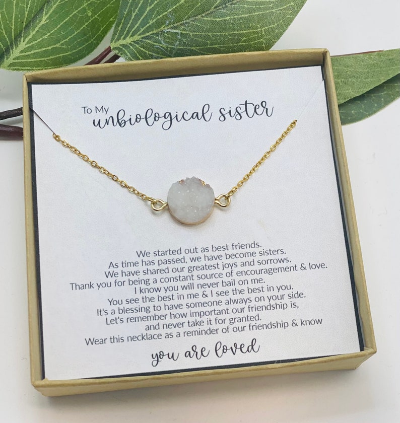 A gold necklace with a white stone on a white card in a brown box
