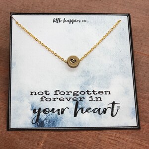 May include: A gold necklace with a small heart charm on a white card with the text "not forgotten forever in your heart".